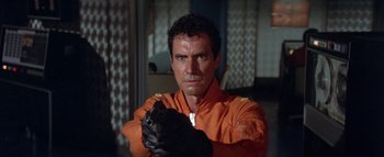 Movie still from “The Swarm” (1978), directed by Irwin Allen – A man in an orange uniform holding a gun; Close Up shot, Low angle