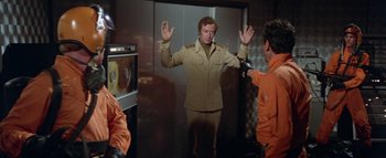 Movie still from “The Swarm” (1978), directed by Irwin Allen – A man standing in front of two other men in an elevator; Medium shot, Over the shoulder angle