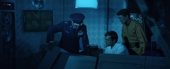 Movie still from “The Swarm” (1978), directed by Irwin Allen – A man sitting in front of another man in a dark room; Medium shot, High angle