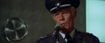 Movie still from “The Swarm” (1978), directed by Irwin Allen – An older man wearing a uniform is speaking into a microphone; Close Up shot, Low angle