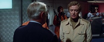 Movie still from “The Swarm” (1978), directed by Irwin Allen – A man in a tan jacket is talking to another man in a black suit; Medium shot, Over the shoulder angle