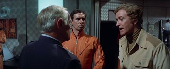 Movie still from “The Swarm” (1978), directed by Irwin Allen – A group of men standing next to each other in a room; Medium shot, Over the shoulder angle