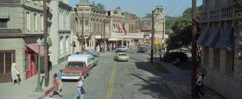 Movie still from “The Swarm” (1978), directed by Irwin Allen – A street scene with cars parked on the side of the road; Extreme Wide shot, High angle