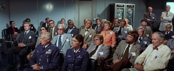 Movie still from “The Swarm” (1978), directed by Irwin Allen – A group of people sitting in chairs in a room; Wide shot, High angle