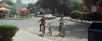 Movie still from “The Swarm” (1978), directed by Irwin Allen – Two young boys are riding their bikes down the street; Wide shot, High angle