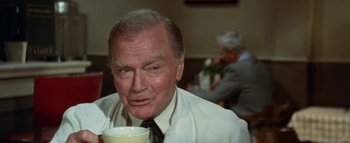 Movie still from “The Swarm” (1978), directed by Irwin Allen – An older man sitting at a table with a cup of coffee; Close Up shot, Over the shoulder angle