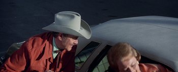 A man wearing a cowboy hat sitting in the back of a car