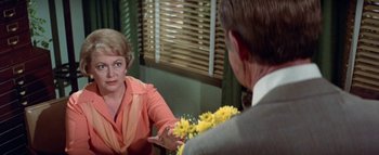 Movie still from “The Swarm” (1978), directed by Irwin Allen – A man and a woman sitting in front of each other holding yellow flowers; Medium shot, Over the shoulder angle