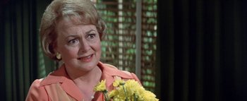 Movie still from “The Swarm” (1978), directed by Irwin Allen – An older woman holding a bouquet of flowers; Close Up shot, Over the shoulder angle