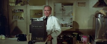 Movie still from “The Swarm” (1978), directed by Irwin Allen – An older man standing in front of a cash register; Medium shot, Over the shoulder angle