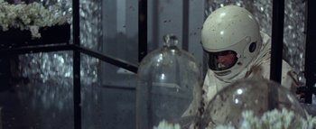 Movie still from “The Swarm” (1978), directed by Irwin Allen – A person wearing a helmet is standing next to a glass jar; Close Up shot, High angle
