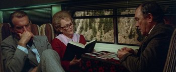Movie still from “The Swarm” (1978), directed by Irwin Allen – An older woman sitting on a train reading a book; Medium shot, High angle