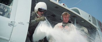 Movie still from “The Swarm” (1978), directed by Irwin Allen – Two people in a helicopter with one of the pilots looking at the camera; Medium shot, Low angle