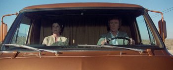 Movie still from “The Swarm” (1978), directed by Irwin Allen – A man and a woman sitting in the drivers seat of an orange car; Medium shot, Low angle