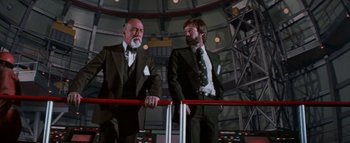Movie still from “The Swarm” (1978), directed by Irwin Allen – A couple of men standing next to each other in suits; Medium shot, Low angle
