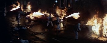 Movie still from “The Swarm” (1978), directed by Irwin Allen – A group of people standing in front of a car on fire; Wide shot, High angle