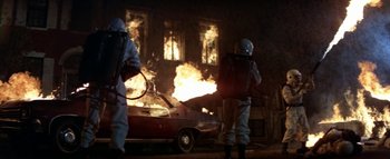 Movie still from “The Swarm” (1978), directed by Irwin Allen – Two men in protective suits spraying a car on fire; Wide shot, Low angle