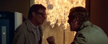 Movie still from “The Swarm” (1978), directed by Irwin Allen – Two men are facing each other in front of fire; Close Up shot, Over the shoulder angle