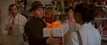 Movie still from “The Truth About Charlie” (2002), directed by Jonathan Demme – A man holding a gift box in front of two other people; Close Up shot, Over the shoulder angle