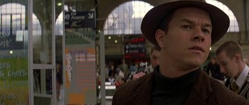 Movie still from “The Truth About Charlie” (2002), directed by Jonathan Demme – A man with a hat is standing in a train station; Close Up shot, Over the shoulder angle
