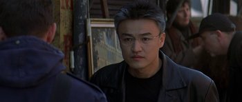 Movie still from “The Truth About Charlie” (2002), directed by Jonathan Demme – A person wearing glasses and a black jacket; Close Up shot, Over the shoulder angle
