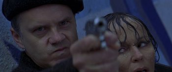 Movie still from “The Truth About Charlie” (2002), directed by Jonathan Demme – A man holding a gun while another man looks on; Close Up shot, Low angle
