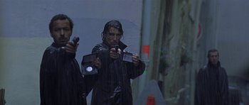Movie still from “The Truth About Charlie” (2002), directed by Jonathan Demme – A man in a black jacket holding a camera; Medium shot, High angle
