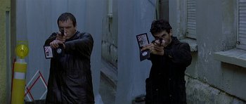 Movie still from “The Truth About Charlie” (2002), directed by Jonathan Demme – Two men in black jackets one holding a cell phone and the other taking a picture; Medium shot, High angle