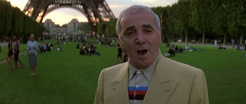 Movie still from “The Truth About Charlie” (2002), directed by Jonathan Demme – An older man in a yellow suit and striped shirt in front of the eiffel tower; Close Up shot, Low angle