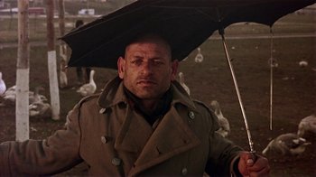 Movie still from “Time of the Gypsies” (1988), directed by Emir Kusturica – A man in a trench coat holding an umbrella over his head; Close Up shot, Low angle