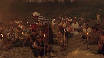 Movie still from “Time of the Gypsies” (1988), directed by Emir Kusturica – A group of people sitting on the ground with lit candles; Wide shot, High angle