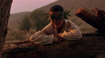 Movie still from “Time of the Gypsies” (1988), directed by Emir Kusturica – A man with a wreath on his head laying on top of a log; Close Up shot, Low angle
