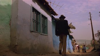 Movie still from “Time of the Gypsies” (1988), directed by Emir Kusturica – A man walking down a street in front of a building; Wide shot, Low angle