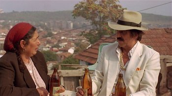 Movie still from “Time of the Gypsies” (1988), directed by Emir Kusturica – A man and a woman sitting at an outdoor table drinking beer; Medium shot, High angle