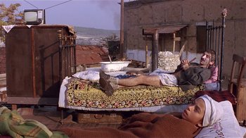 Movie still from “Time of the Gypsies” (1988), directed by Emir Kusturica – A man laying on a bed in the middle of the day; Wide shot, High angle