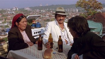Movie still from “Time of the Gypsies” (1988), directed by Emir Kusturica – A group of people sitting at a table with beer; Medium shot, High angle