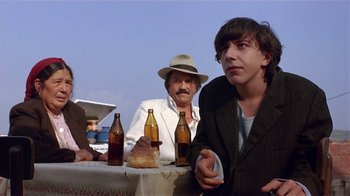Movie still from “Time of the Gypsies” (1988), directed by Emir Kusturica – A group of people sitting at a table with beer; Medium shot, Low angle