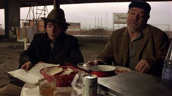 Movie still from “Time of the Gypsies” (1988), directed by Emir Kusturica – Two men sitting at a table with a bowl of food; Medium shot, Low angle