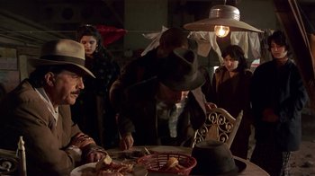 Movie still from “Time of the Gypsies” (1988), directed by Emir Kusturica – A group of people standing around a table; Medium shot, Over the shoulder angle