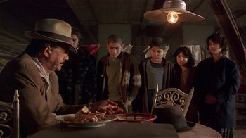 Movie still from “Time of the Gypsies” (1988), directed by Emir Kusturica – A group of people standing around a table with food on it; Medium shot, Over the shoulder angle