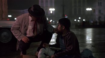 Movie still from “Time of the Gypsies” (1988), directed by Emir Kusturica – A man in a suit and a man in a hat and bandage on the street; Medium shot, Over the shoulder angle