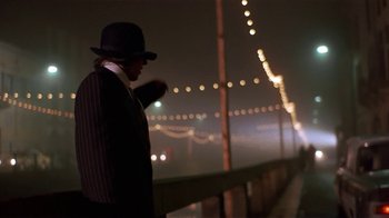 Movie still from “Time of the Gypsies” (1988), directed by Emir Kusturica – A man wearing a hat and a suit standing on a bridge at night; Wide shot, Low angle