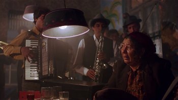 Movie still from “Time of the Gypsies” (1988), directed by Emir Kusturica – An older woman sitting at a table with a lamp hanging from the ceiling; Medium shot, Low angle