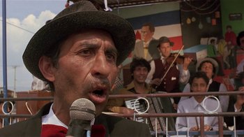 Movie still from “Time of the Gypsies” (1988), directed by Emir Kusturica – A man with a microphone in front of a picture of a man with a microphone; Close Up shot, Low angle