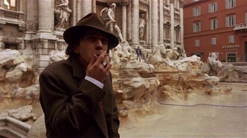 Movie still from “Time of the Gypsies” (1988), directed by Emir Kusturica – A man wearing a hat smoking a cigarette in front of a building; Medium shot, Low angle