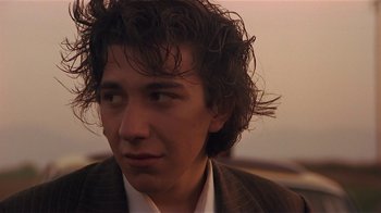 Movie still from “Time of the Gypsies” (1988), directed by Emir Kusturica – A young man with long brown hair wearing a suit; Close Up shot, Low angle