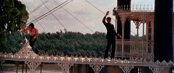 Movie still from “Tom Sawyer” (1973), directed by Don Taylor – A man standing on top of a bridge waving; Wide shot, Low angle