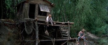 Movie still from “Tom Sawyer” (1973), directed by Don Taylor – A person sitting on the side of a house on a wooden platform; Wide shot, High angle