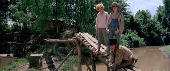 Movie still from “Tom Sawyer” (1973), directed by Don Taylor – A group of people standing on top of a wooden bridge; Wide shot, Low angle