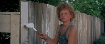 Movie still from “Tom Sawyer” (1973), directed by Don Taylor – A young boy holding a paintbrush in front of a wooden fence; Medium shot, Low angle